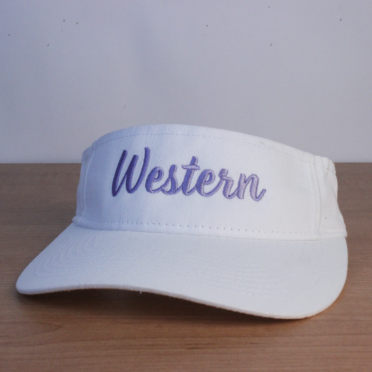 White visor with Western cursive script embroidered in lavender lettering.