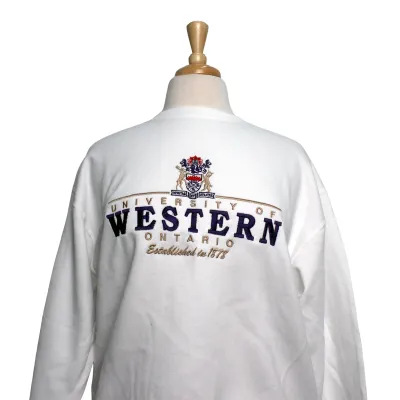 White crewneck with a vintage coat of arms and heritage style script embroidered on the front. 
