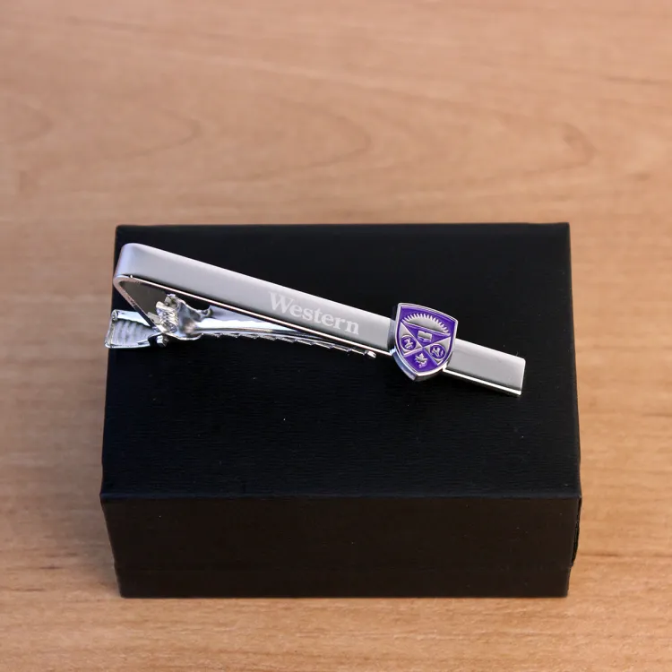 Silver tie bar with a western crest embellishment displayed on top of a ring box.