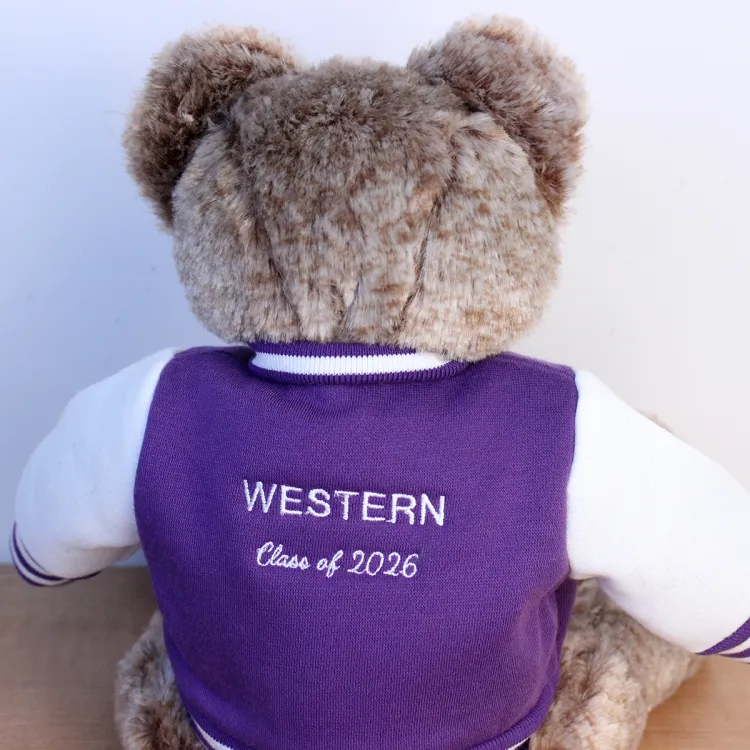 Brown teddy bear with a purple and white letterman jacket that shows "Western Class of 2026" on the back of the jacket.